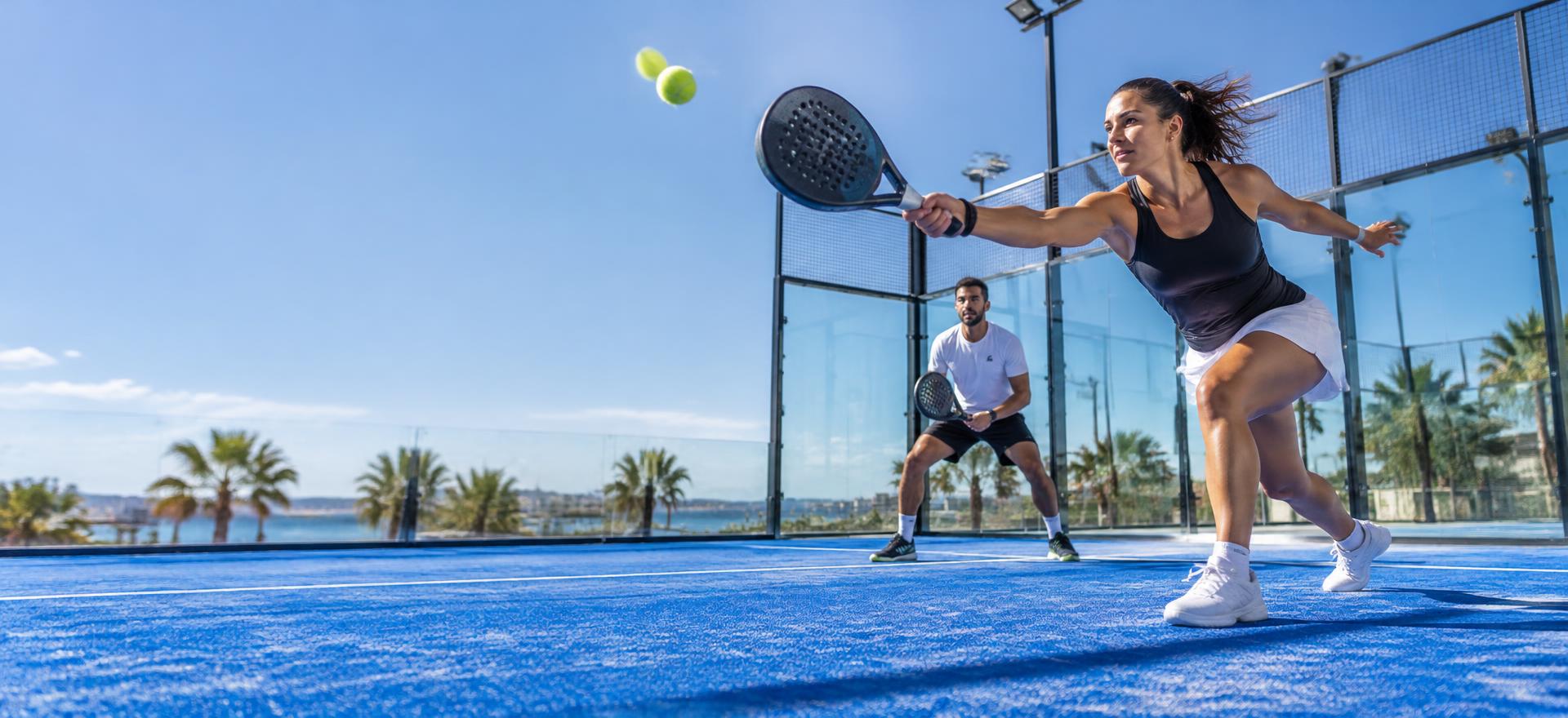 Twee padelspelers in actie op een blauwe padelbaan in de zon